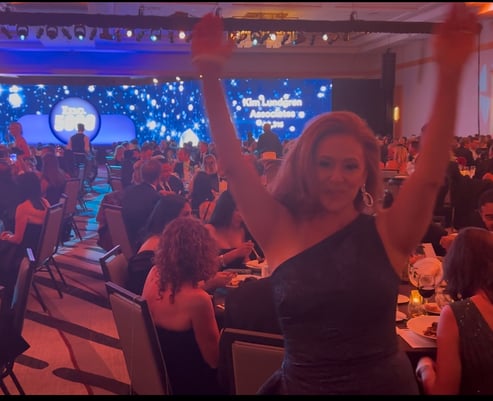 Woman in dress holding her hands up in celebration in crowded ballroom